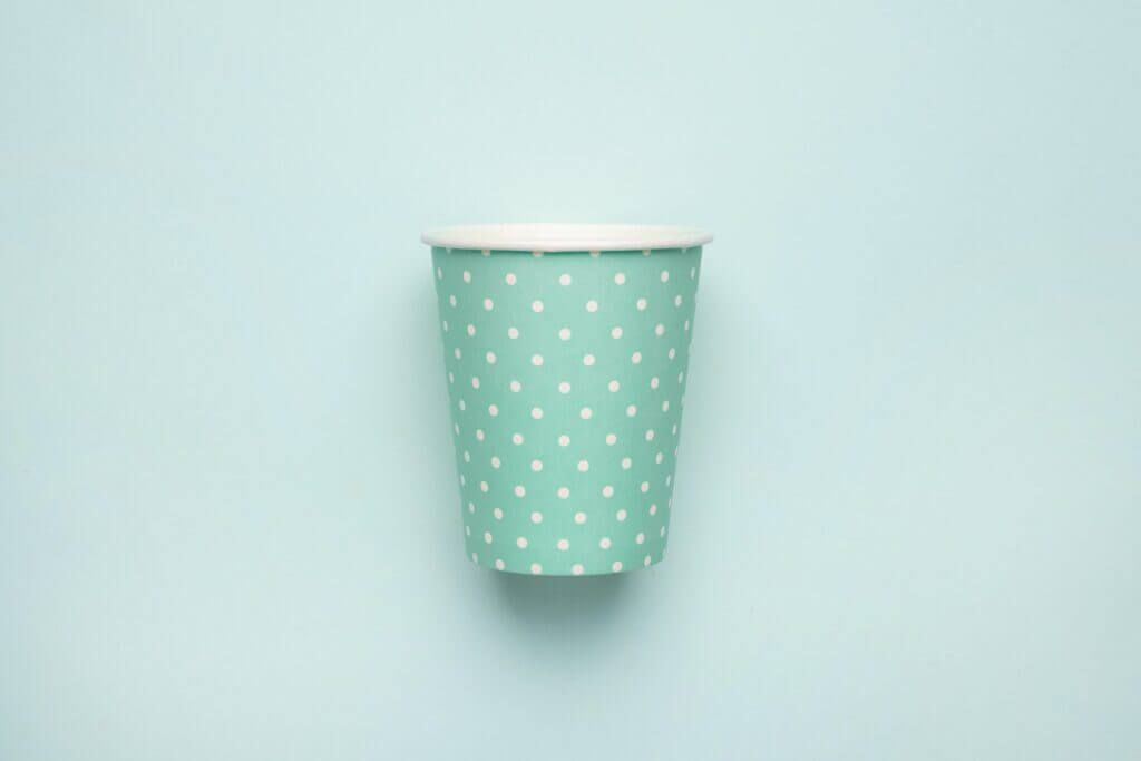 Paper cup with polka dot print green color on mint background. Eco friendly takeout cup for drink
